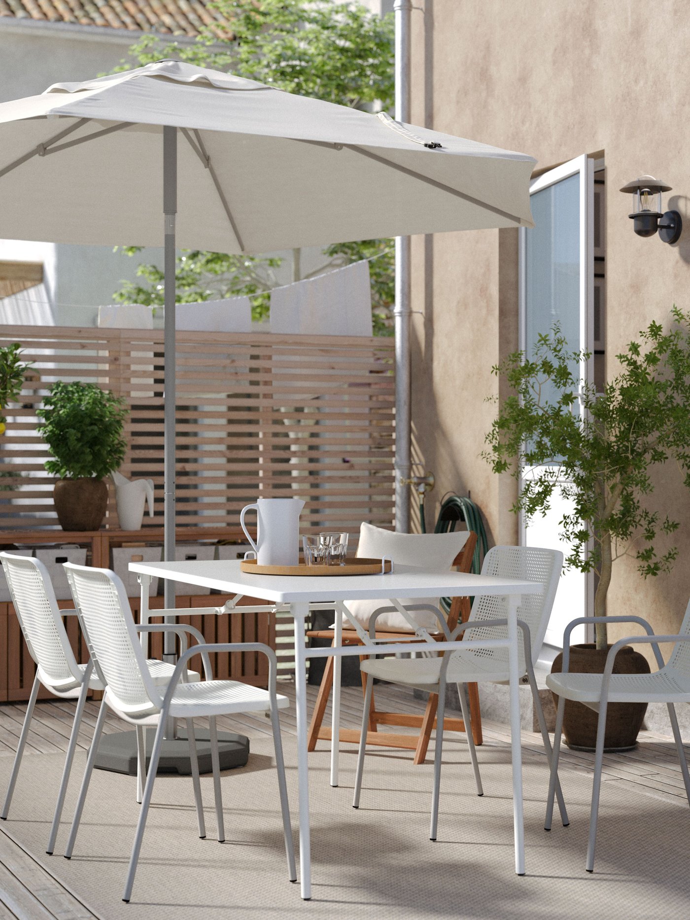 Klappbarer TORPARÖ Tisch und 4 passende Gartenstühle mit Armlehnen auf einer Terrasse. Dahinter steht ein Sonnenschirm. 