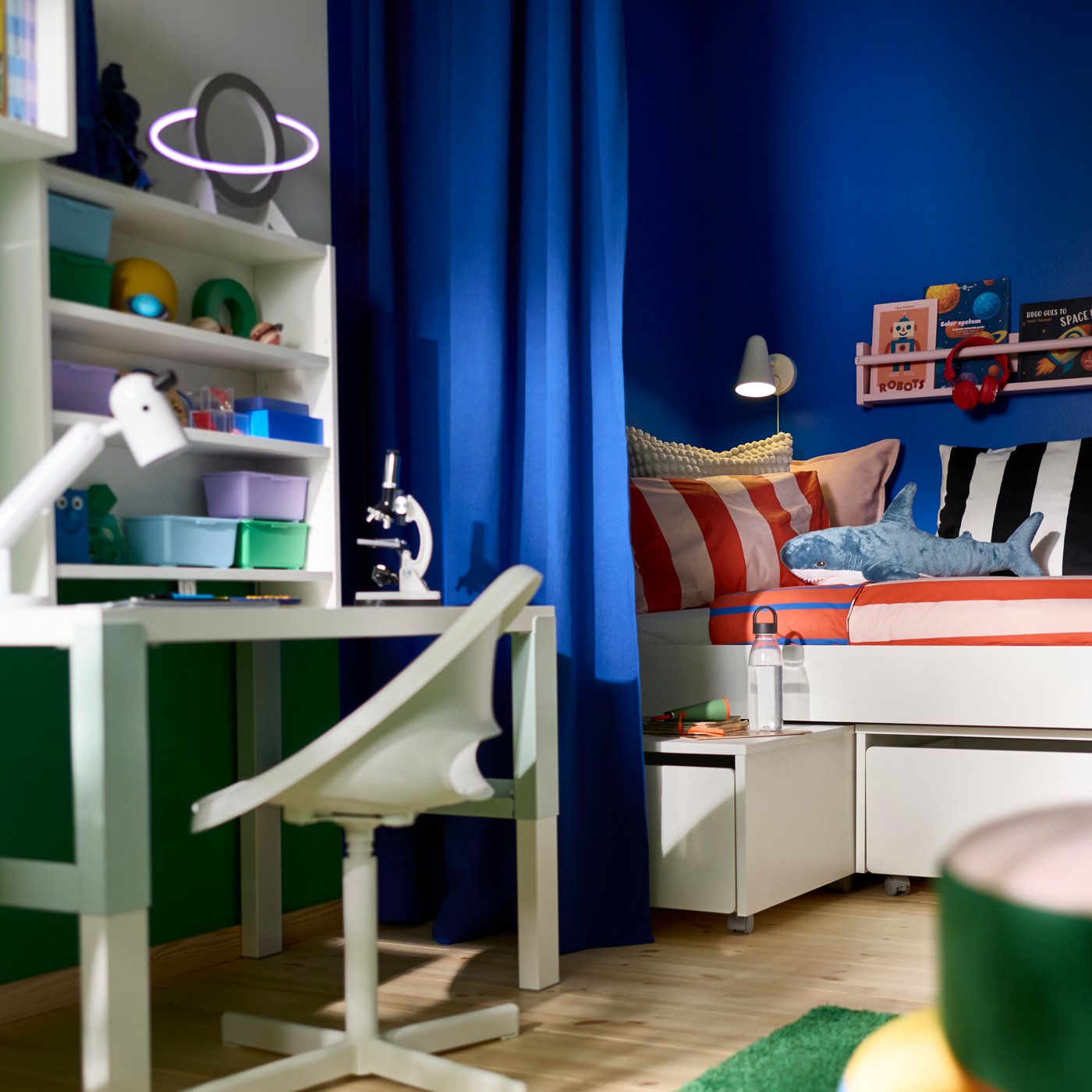 Blue GINSTMOTT curtain hanging beside a children’s desk and bed in a room with shelving, storage units and study accessories.