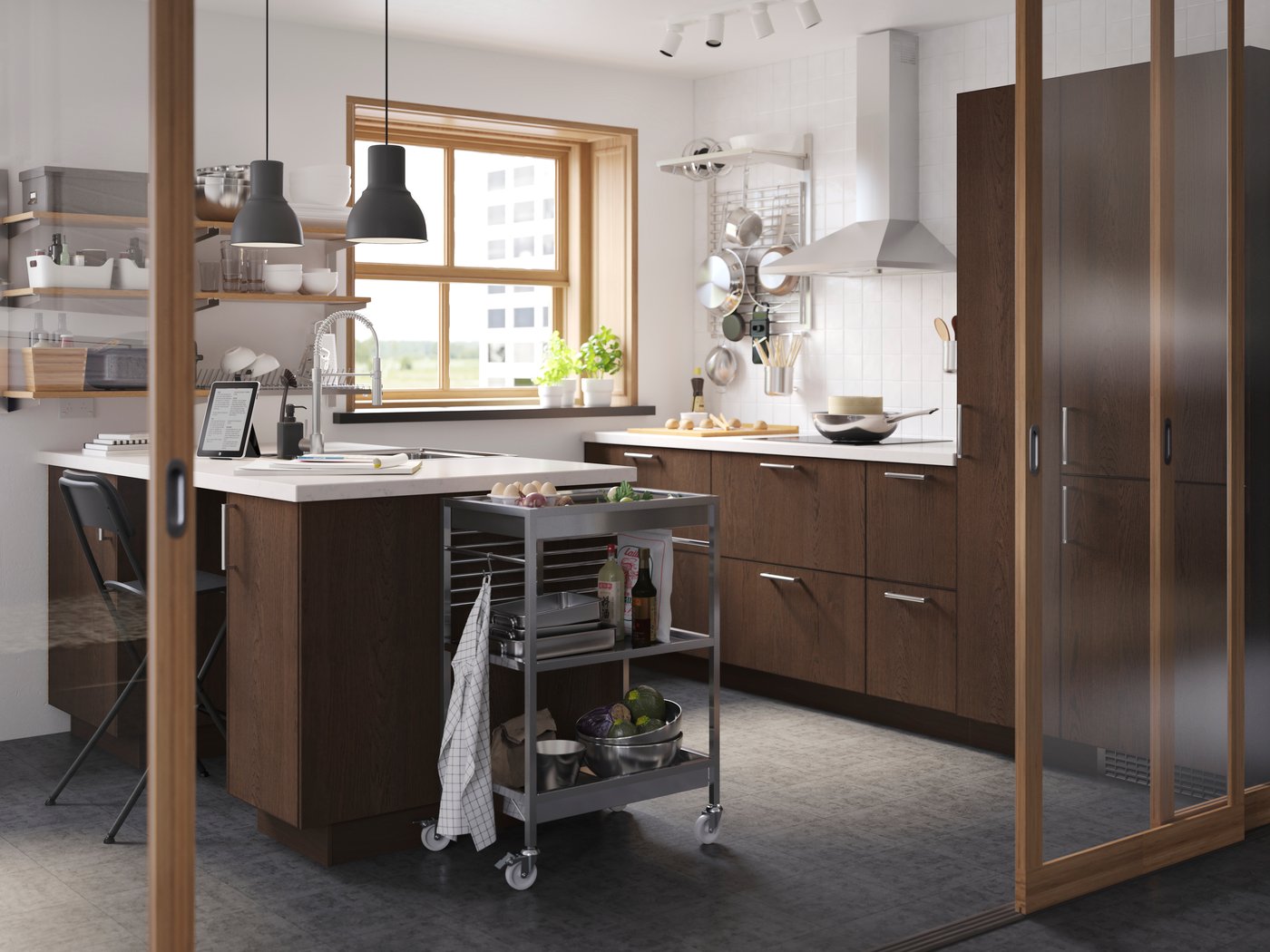 Cucina a vista in un ambiente ben illuminato con cassetti e ante SINARP, cappa in alluminio, lampade a sospensione nere e carrello KUNGSFORS a lato.
