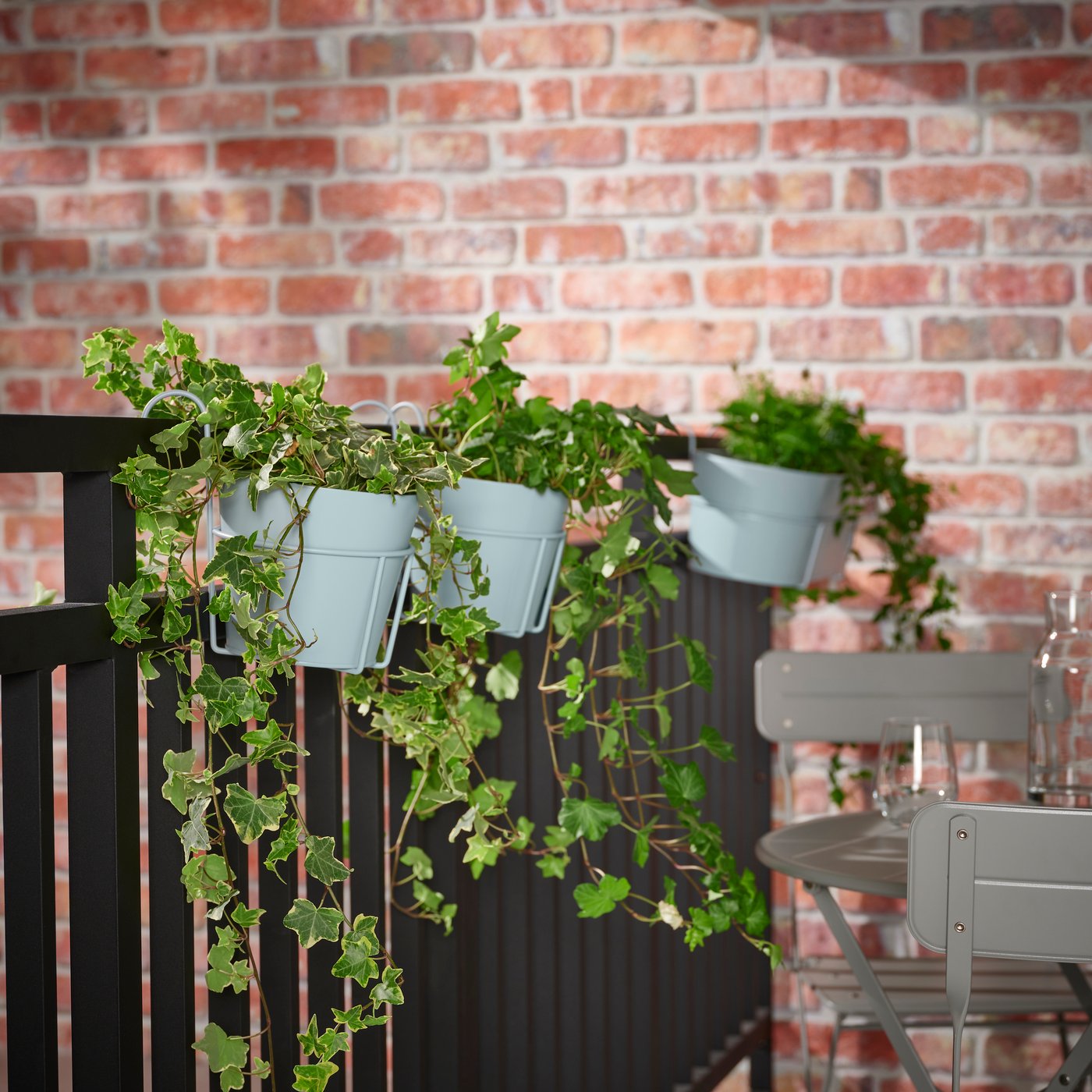 An in/outdoor light grey-blue VITLÖK plant pot with holder hanging on the balcony railing.