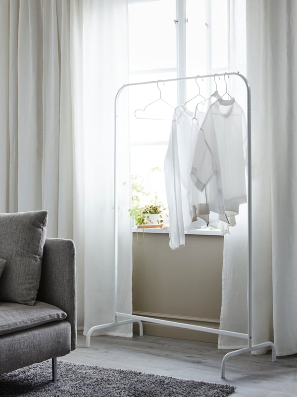 A white, transparent curtain separates a sofa from a grey-green NIKKEBY clothes rack with shoes, clothes and accessories.