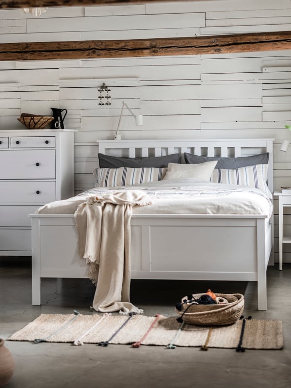 Ein weißes HEMNES Doppelbett steht in einem hellen Schlafzimmer. Daneben steht eine HEMNES Kommode in weiß mit 6 Schubladen. 