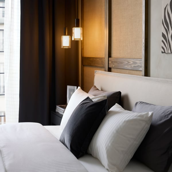 A hotel bed has rows of pillows and white, sateen-woven NATTJASMIN duvet cover and pillowcases that are discreetly striped.