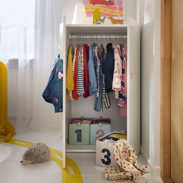 Hanging children’s clothes and labelled storage boxes in a low LASTARE wardrobe combination set in a light-filled kids’ room.