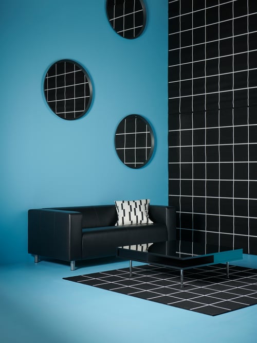Modern interior with black sofa, glossy black coffee table, flat woven rug, mirror and cushion cover.