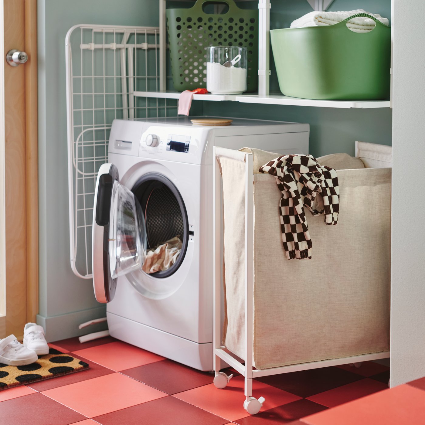 An 80-liter ENHET laundry bag with castors has a shirt hanging out the top and is by a washing machine with its door open.