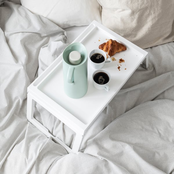 White KLIPSK tray with coffee and food on a plush white bed.