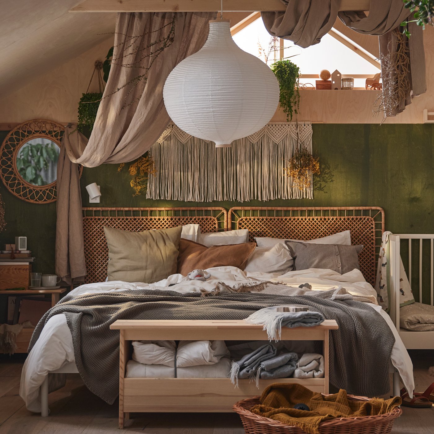 Schlafzimmer in Boho-Optik mit einem Doppelbett, u. a. mit neutralfarbener Bettwäsche, Kissen und einem GULLIVER Babybett daneben.