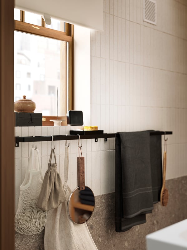 A SKOGSVIKEN towel rail has some towels hanging on it, and also some hooks with different bathroom items hanging from them.