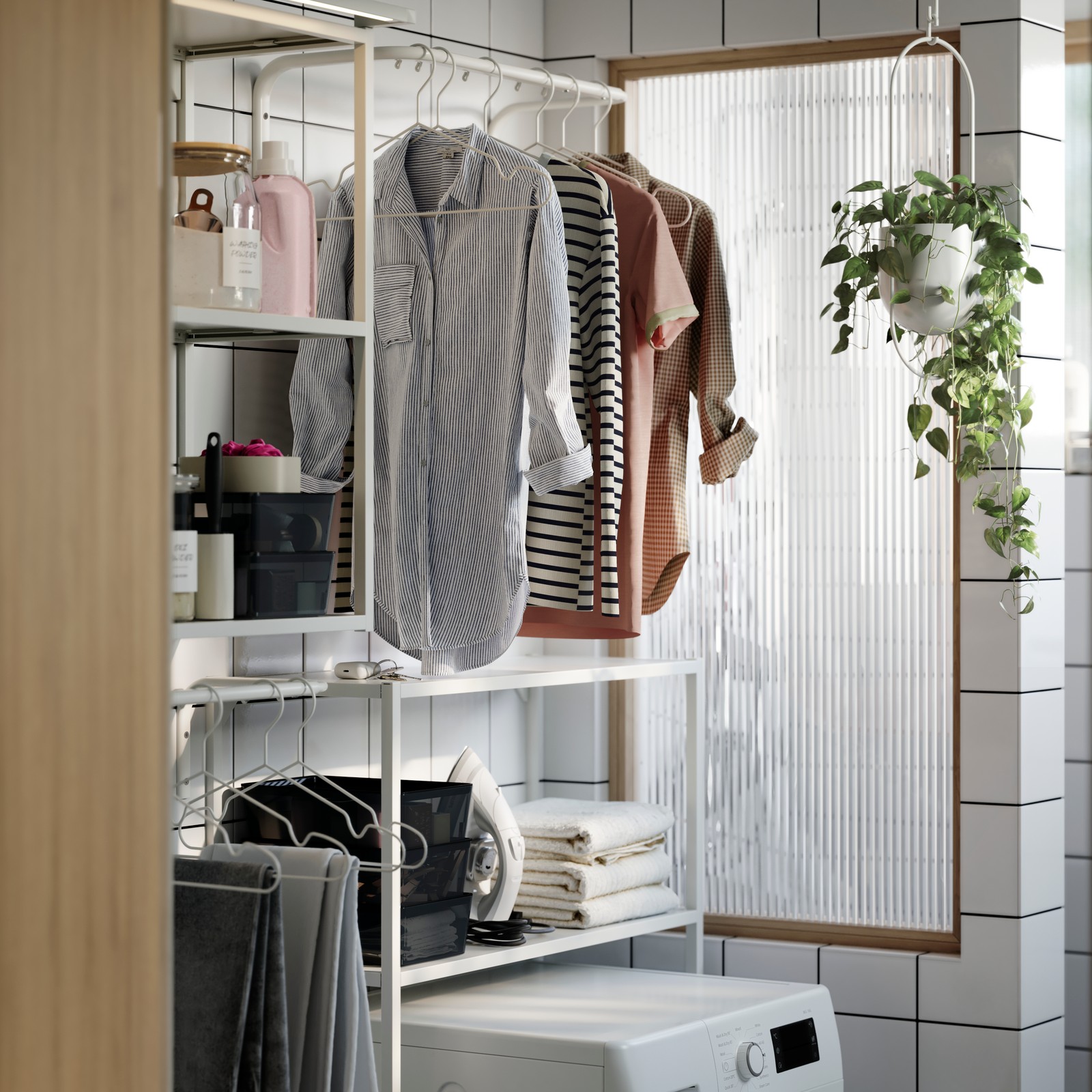 A modern laundry nook with a white ENHET frame of two shelves above and around a washing machine. Shirts hanging on a rail.