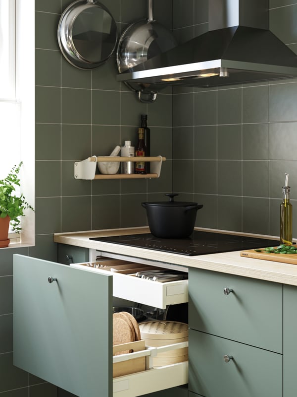 A drawer in a kitchen cabinet with a grey green NICKEBO front has been pulled out and there are kitchen utensils inside.