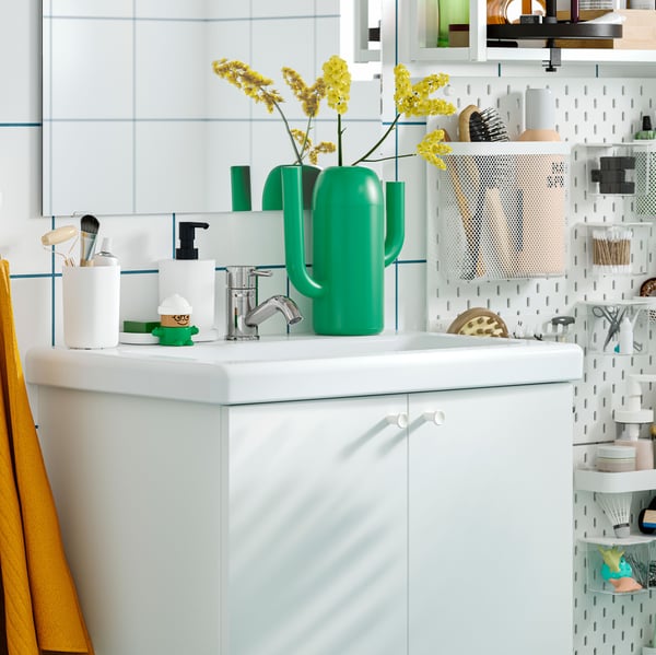 A white ENHET base cabinet with a white washbasin is mounted on a white-tiled bathroom wall next to a white SKÅDIS pegboard.