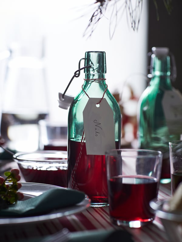 A section of a table set with drinks in VINTER 2021 bottles, decorations and a beige-and-red VINTER 2021 tablecloth.