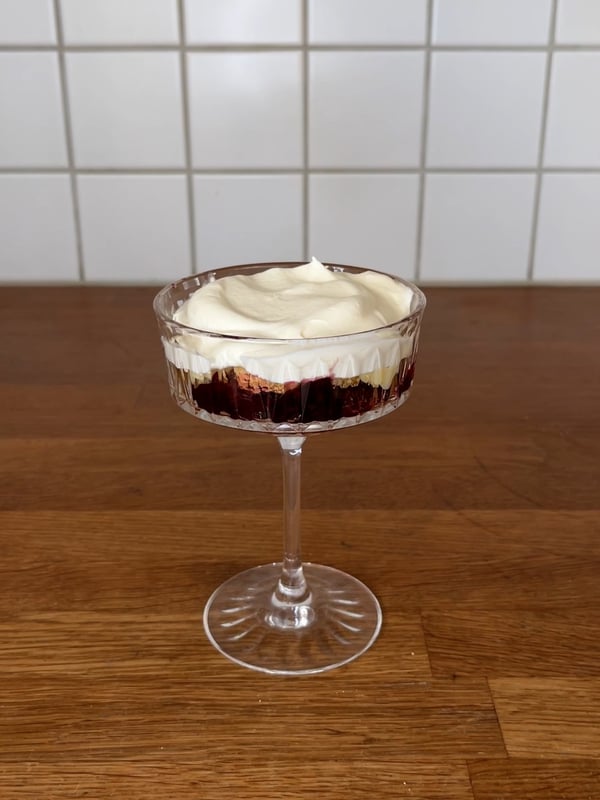 En champagnecoupe med tårtbotten, sylt, vaniljkräm och vispad grädde i.