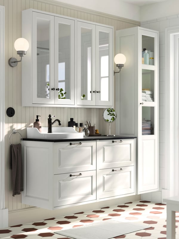 Dans une salle de bain au sol carrelé en blanc et brun, deux meubles lavabos TÄNNFORSEN avec tiroirs et un plateau noir.