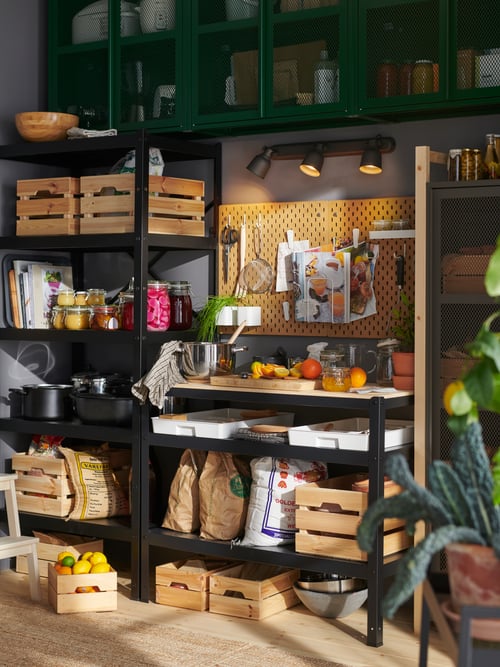 A pantry wall with the green mesh IVAR cabinet with doors and black BROR work bench holding pine KNAGGLIG boxes and produce.