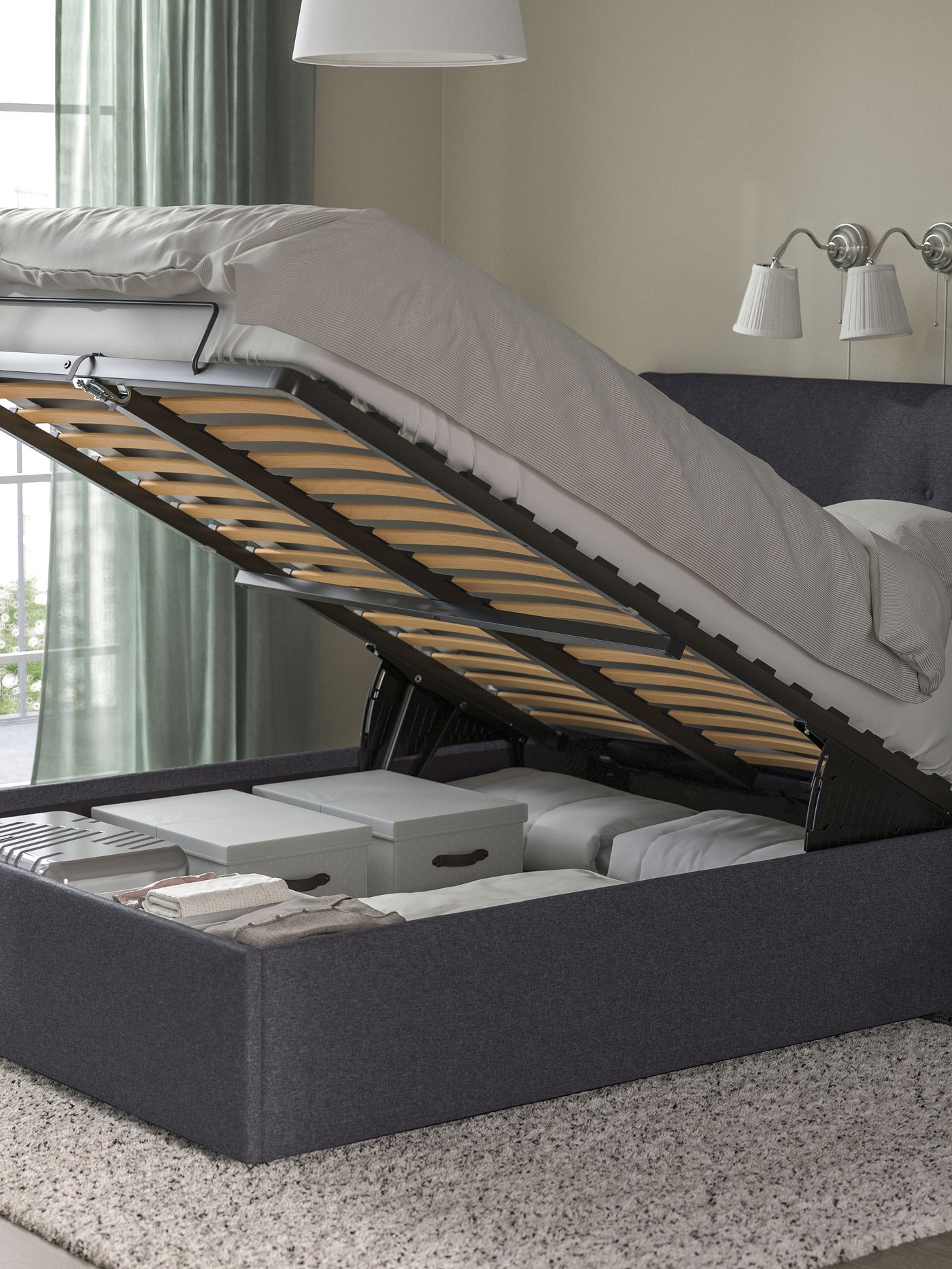 A grey IDANÄS bedframe with storage, which is open, showing everything inside.