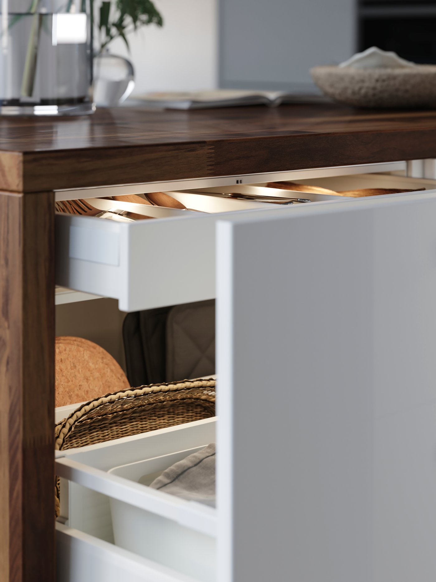 A drawer in a kitchen cabinet with white fronts and drawer lighting is pulled out and there are kitchen items stored inside.