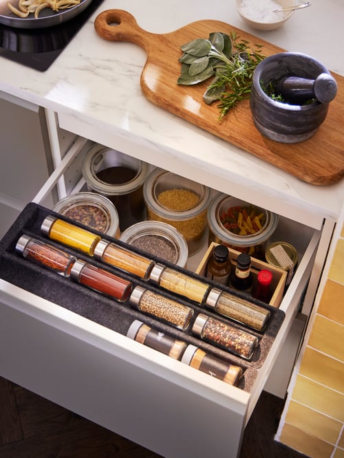 A UPPDATERA sliding organiser for drawer filled with jars and spice jars. Above it, a chopping board and a pestle and mortar.