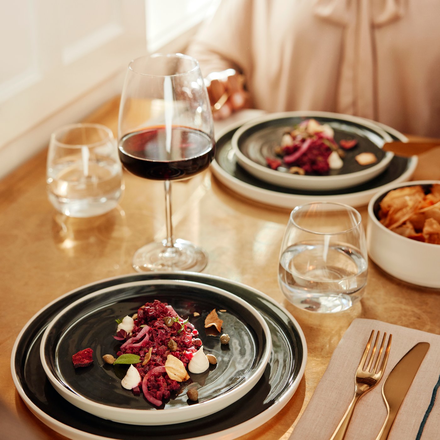 Green plates with colourful salads served on them are placed on a light brown table with DYRGRIP glasses for wine and water.