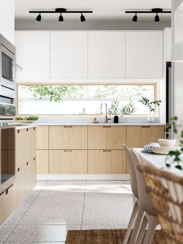 A kitchen and dining area with windows facing a garden. FRÖJERED fronts, in bamboo, are combined with fronts in white.