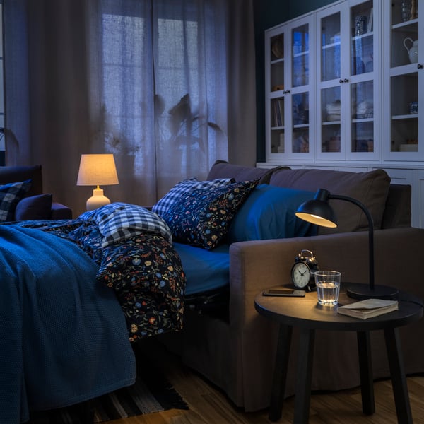 A HYLTARP sofa-bed, configured as a bed and with BRUDKRUSBÄR bed linen, stands in front of some HAVSTA storage combinations.