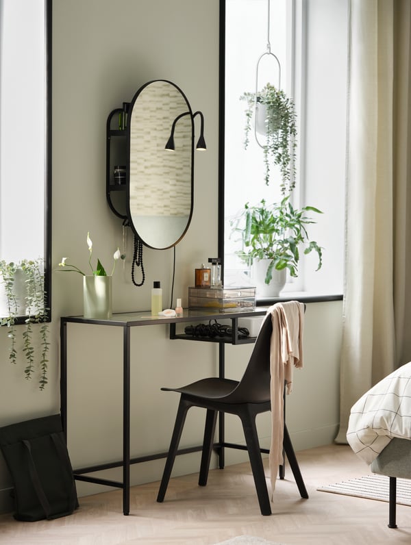 Ein schwarzer VITTSJÖ Laptoptisch mit Glasplatte der in einem Schlafzimmer als Schminktisch an der Wand steht. Davor ein Stuhl und darüber ein Spiegelschrank. 