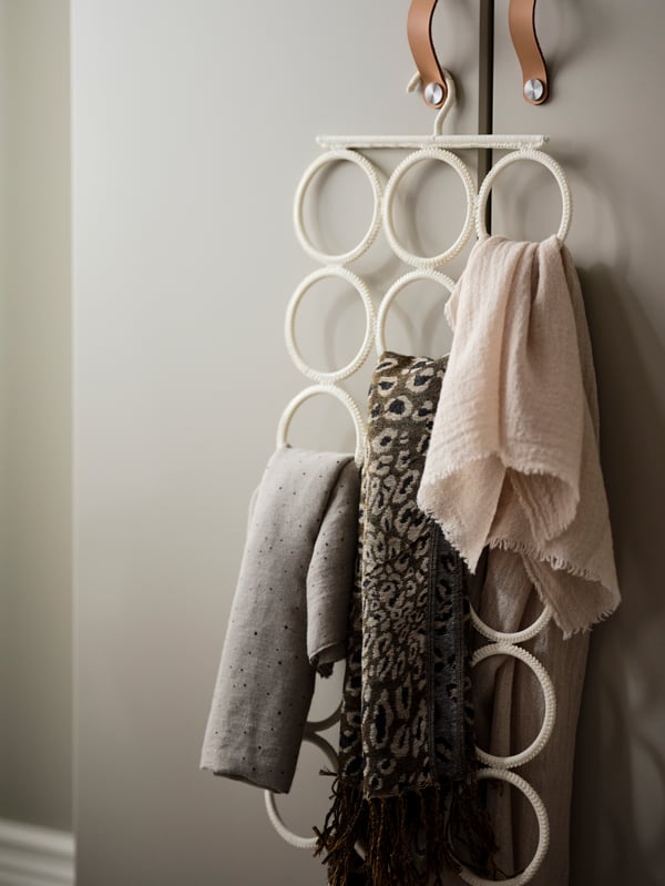 A white KOMPLEMENT multi-use hanger holding some scarves hangs from a handle of a wardrobe.