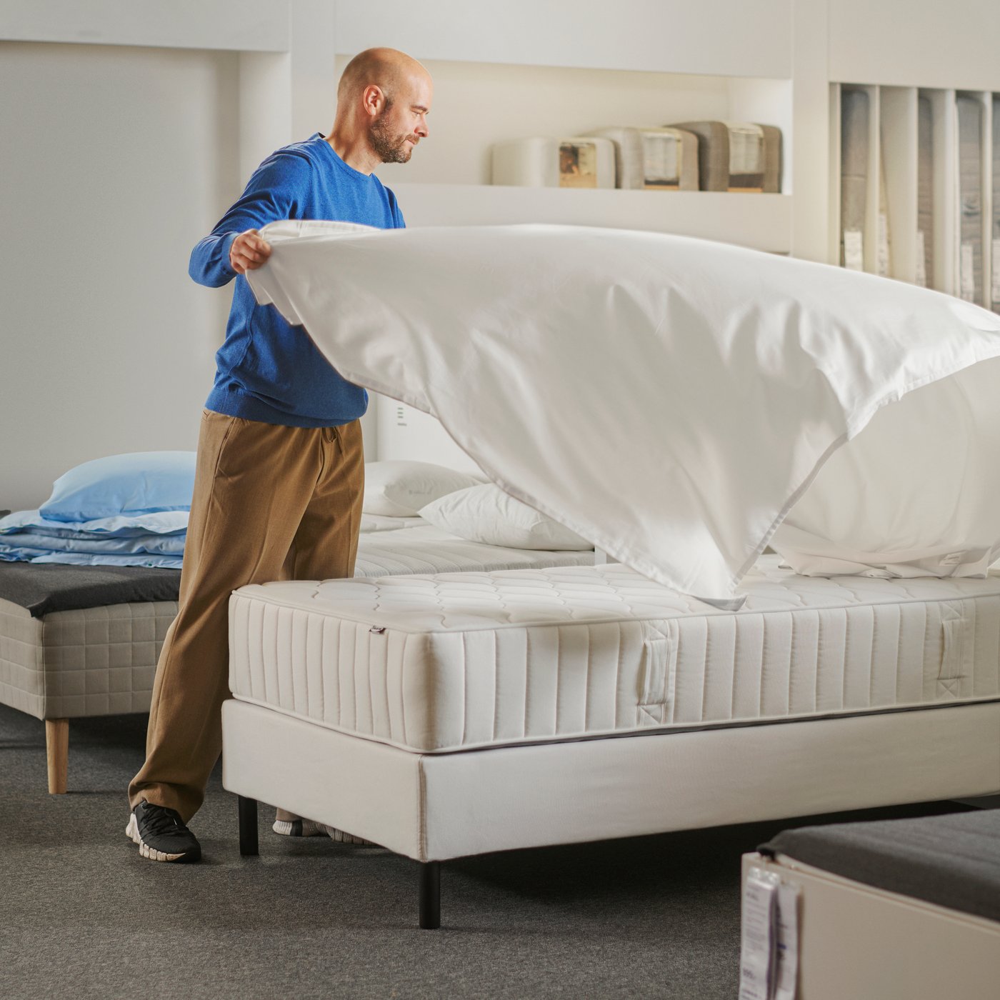 A person covering a VÅGSTRANDA pocket sprung mattress with a bedsheet in a store setting.