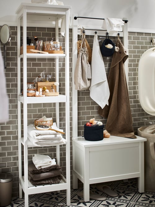 Stylish bathroom with white wooden shelving unit holding towels and accessories and storage bench with towel rail.