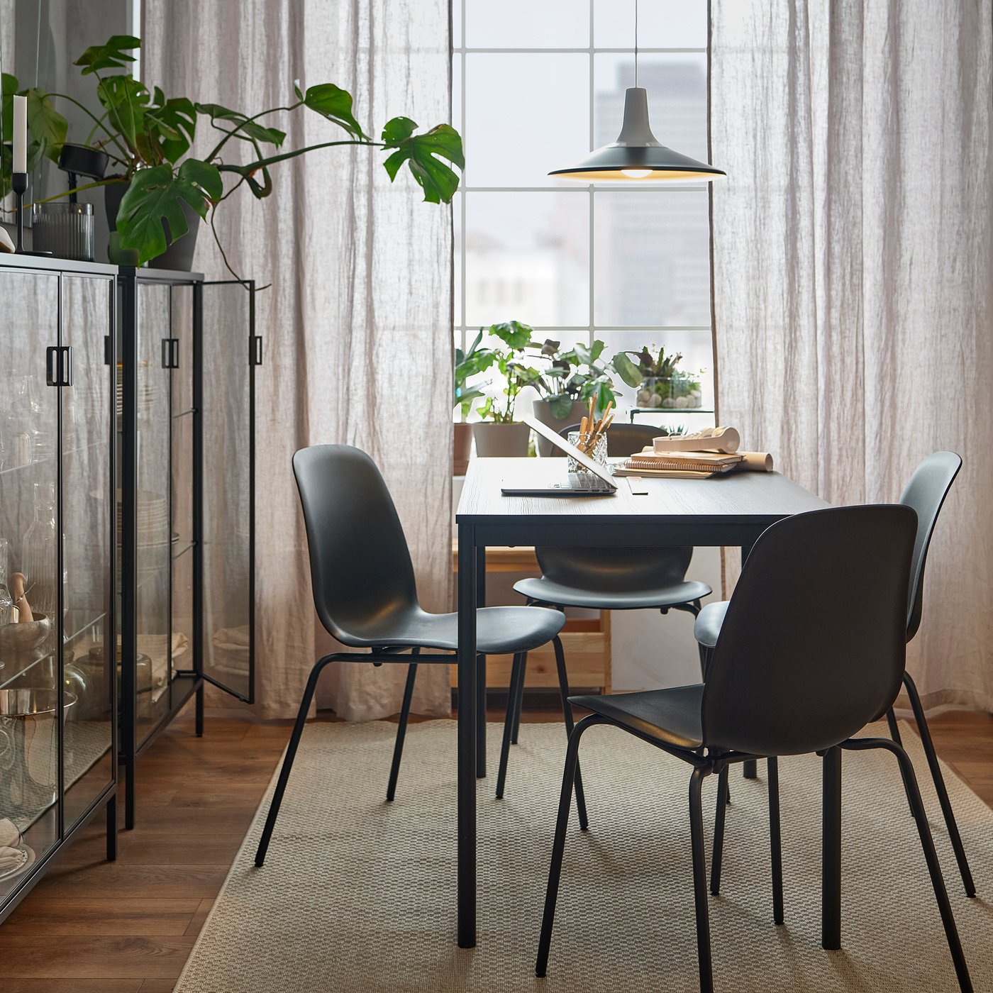 Två svarta RUDSTA glasskåp står vid väggen och ljuset strömmar in på ett svart SANDSBERG matbord och LIDÅS stolar.