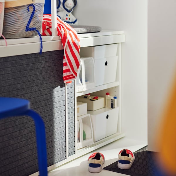 The bottom of a PLATSA open wardrobe with one sliding cupboard door open showing various white storage boxes and toys inside.