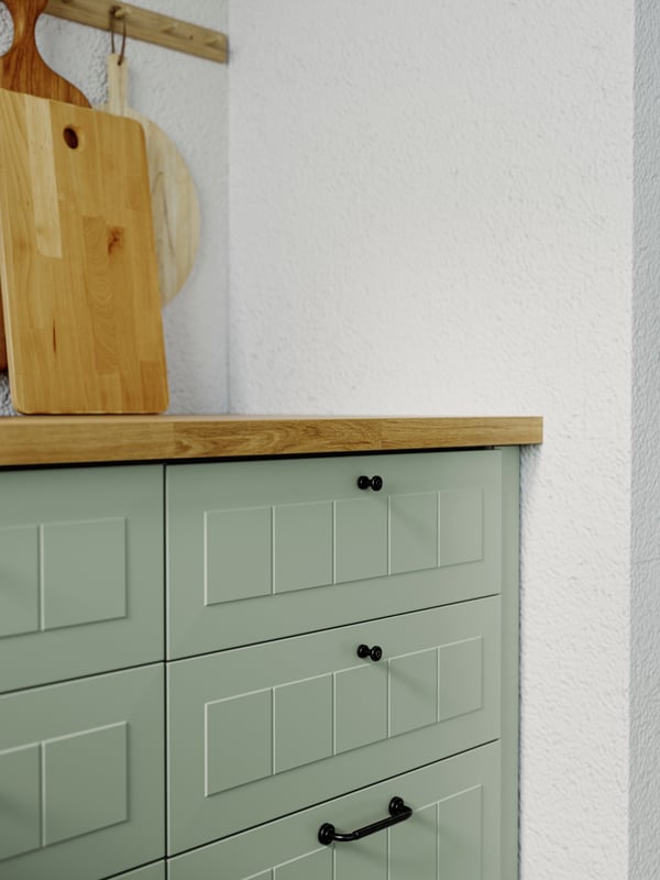 A kitchen corner with STENSUND drawer fronts in light green with a wooden worktop that has a wooden chopping board on it.