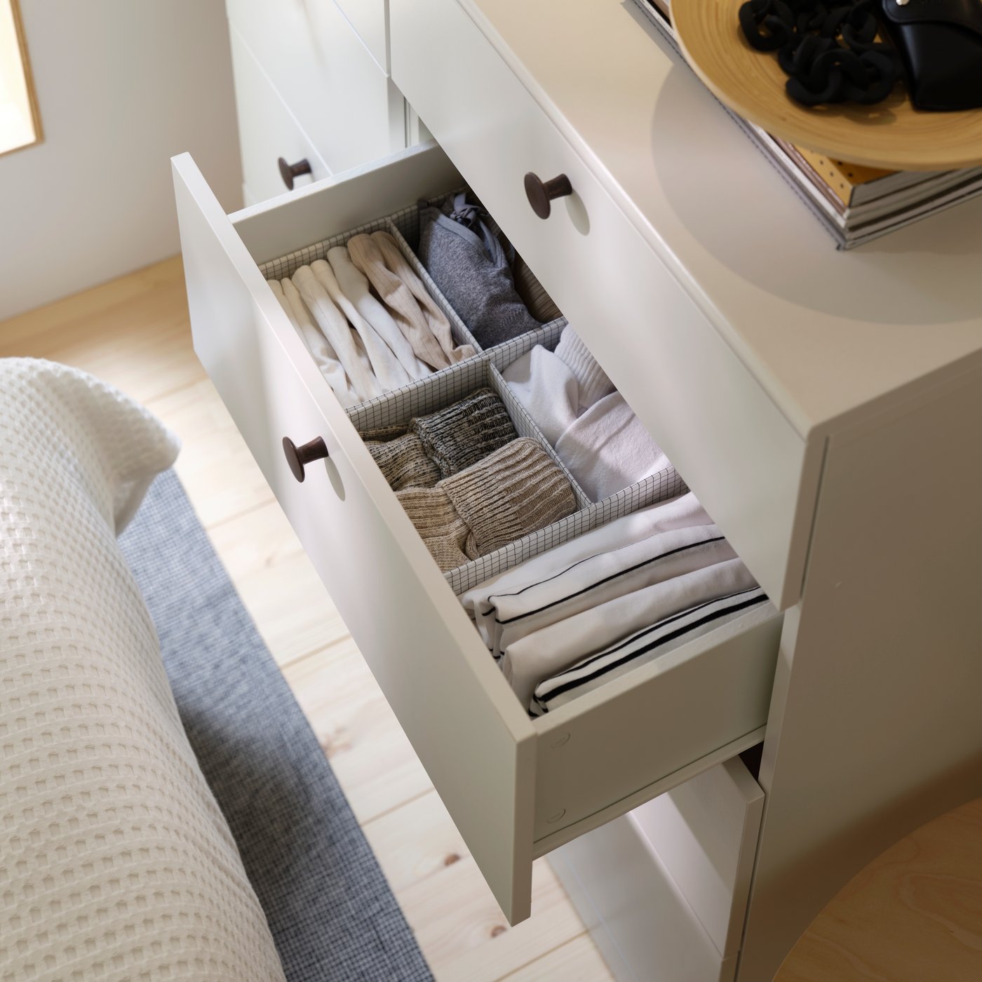An open drawer revealing a STUK box with compartments organising folded clothes inside a white chest of drawers.