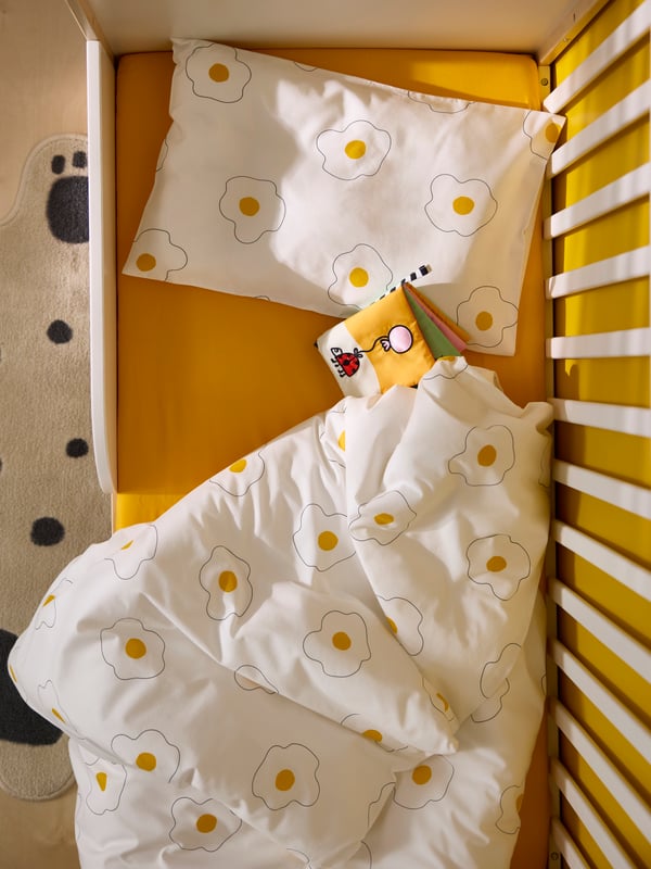 Ein Babybett ist aus der Vogelperspektive zu sehen, darin liegt eine ÖGONLOCKSMAL Babybettwäsche