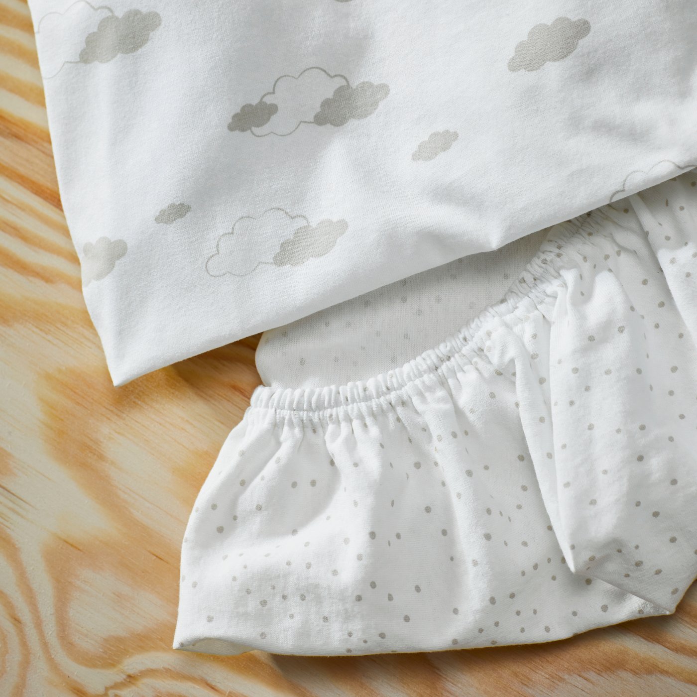 Two ÄLSKVÄRD fitted sheets for bassinet, one with dots and one with clouds, on a wooden surface.