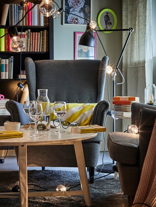 A seating area with a front view of a STRANDMON wing chair in Nordvalla dark grey behind a coffee table with drinks on it.