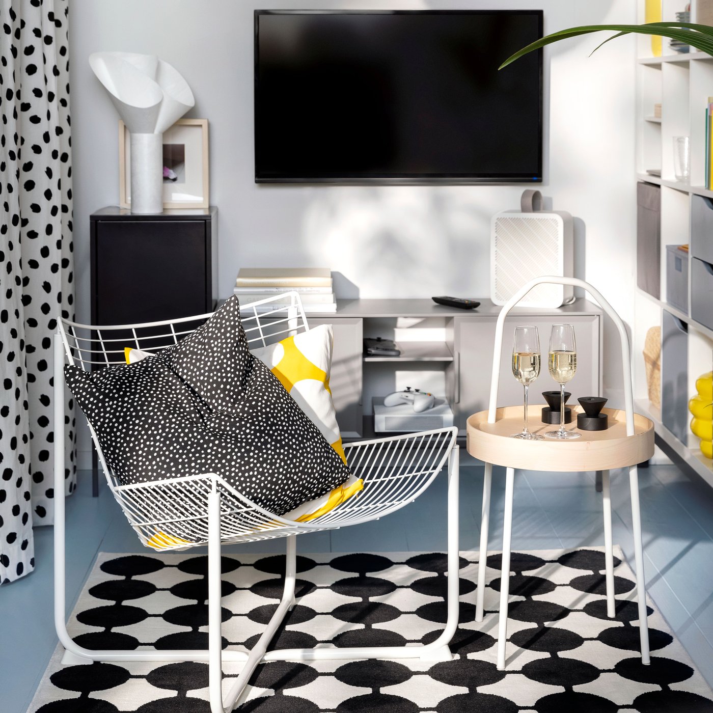 A white SKÅLBODA armchair and a BURVIK side table stand on a black and white VÄNDPLATS rug in a small living room area.