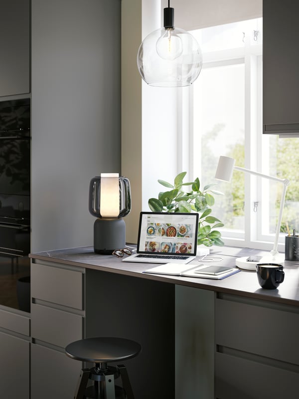 A black SYMFONISK table lamp on a desk next to a laptop.