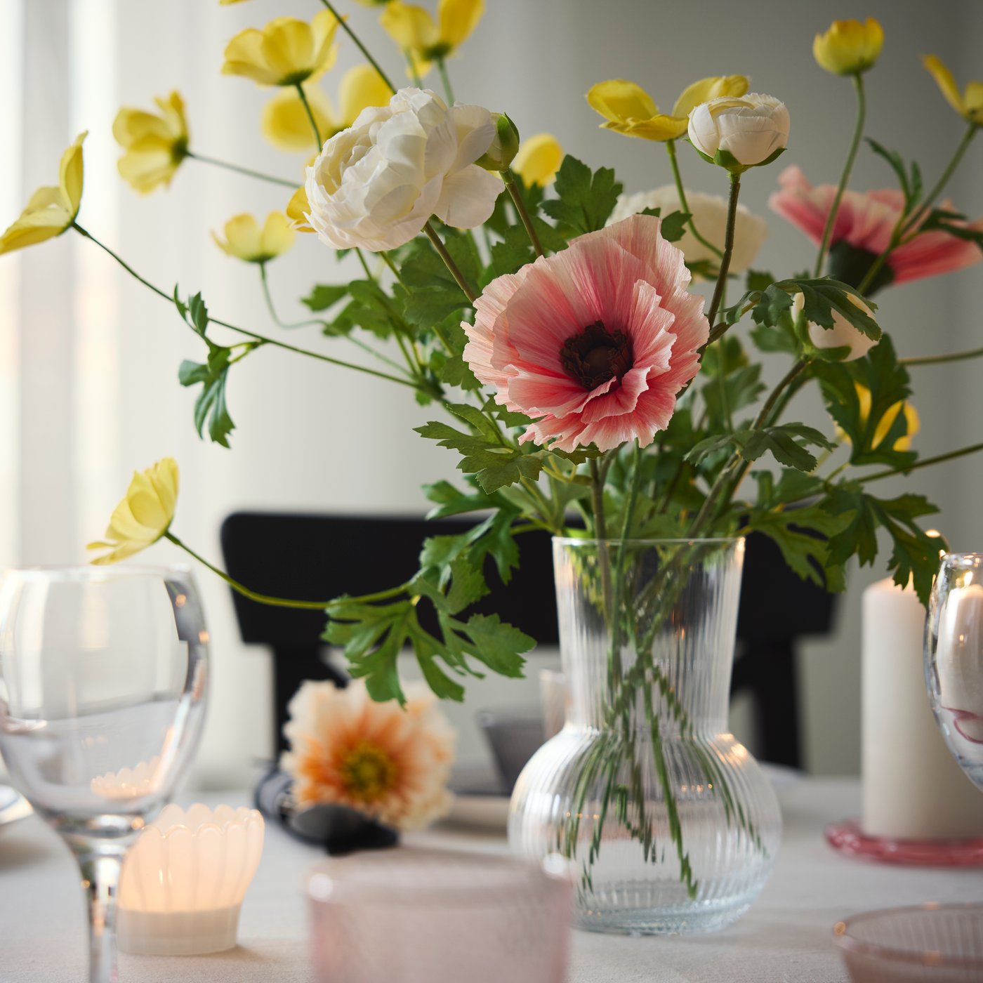 A dining table with a clear vase holds artificial flowers including pink GULDSPETT artificial flowers made of paper.