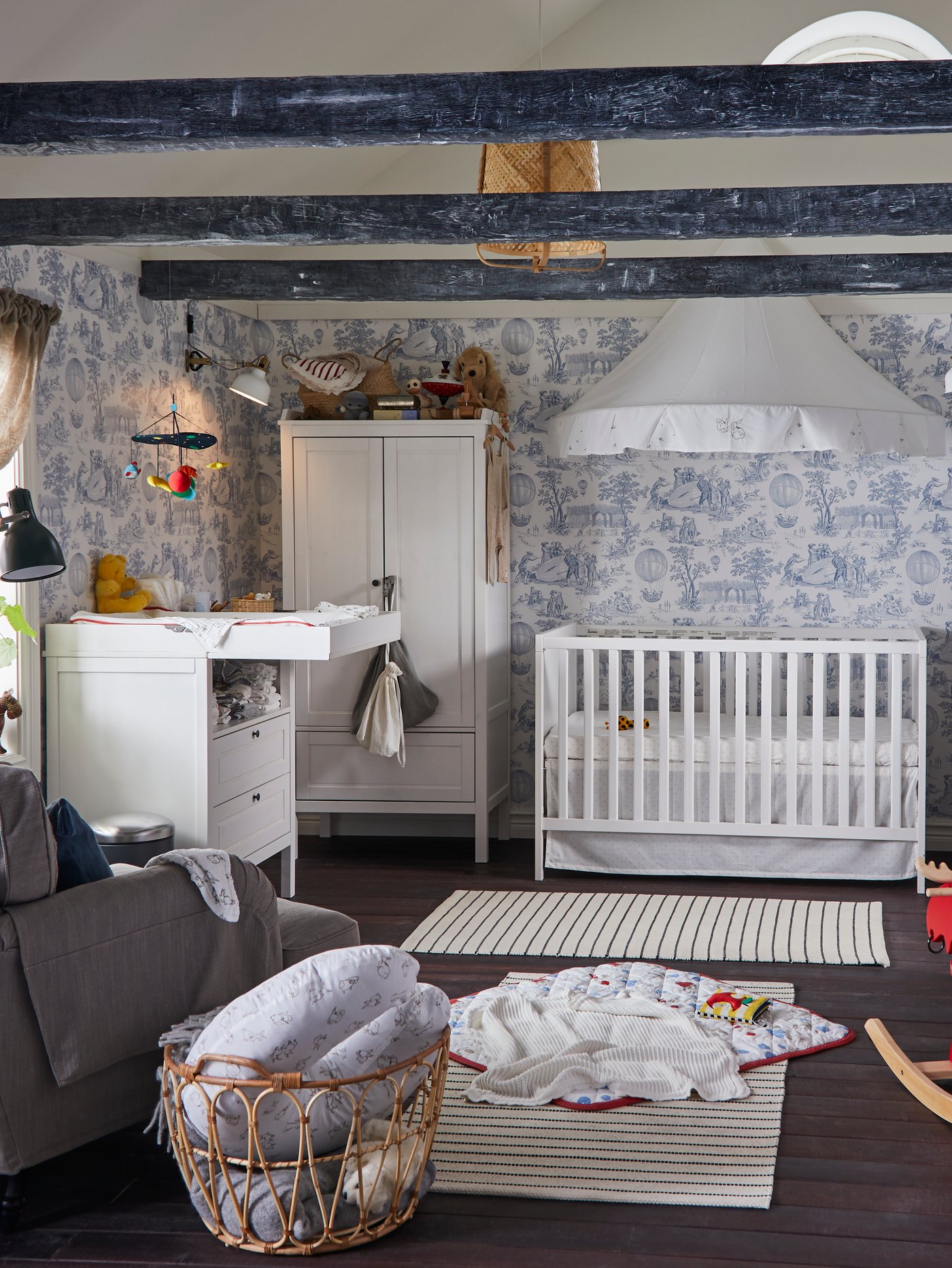 Ein traditionelles Babyzimmer mit weißem Kleiderschrank, Babydecke, Spielbereich, Leseleuchte und Wickeltisch.