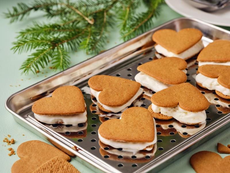 Gelati al pan di zenzero a forma di cuore posti su un vassoio in acciaio uno accanato all'altro. Dietro, un ramo di pino.