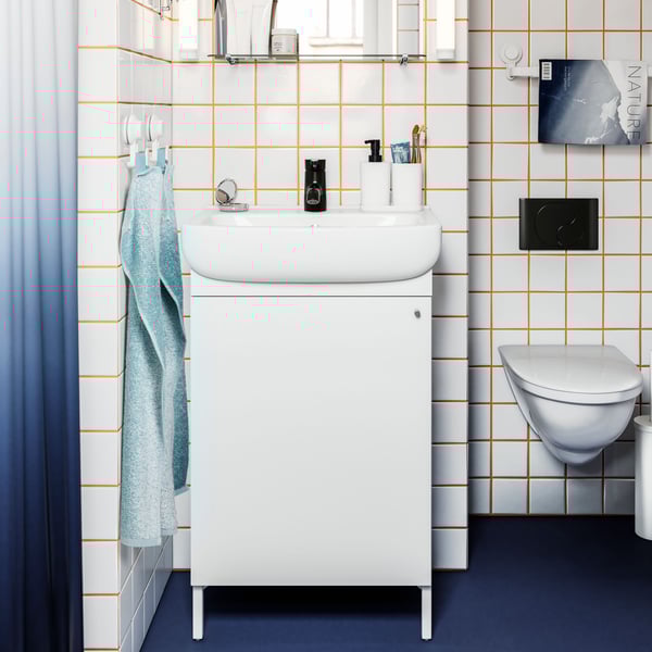 A bathroom with white tiles and orange grout lines featuring a NYSJÖN vanity sink cabinet and a NYSJÖN mirror with shelf.