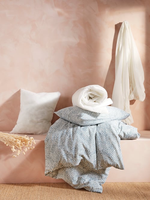 Pastel orange wall and bed with two pillows, one with pillowcase, one without, quilt cover, duvet and throw.