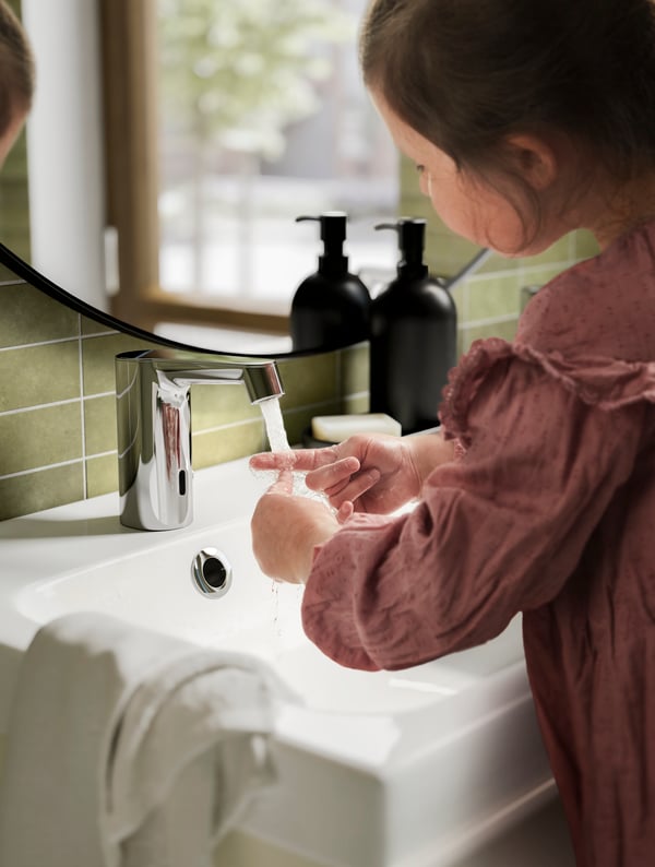 Una niña frente a un espejo de baño jugando con el agua del grifo.