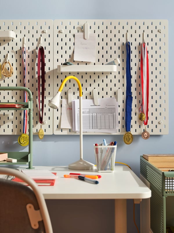 Two white SKÅDIS pegboards with hooks, clips and shelves from the range holding medals, papers and other small items.