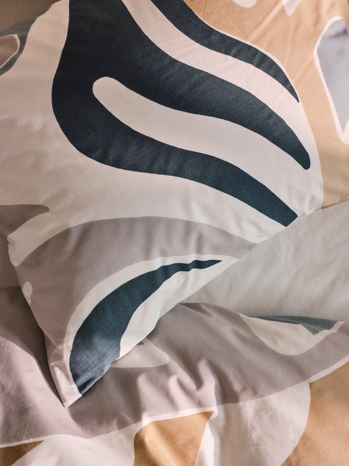 A close-up of a duvet with a pillow on top, both covered in a MYGGLASVINGE multicolour duvet cover and pillowcase.