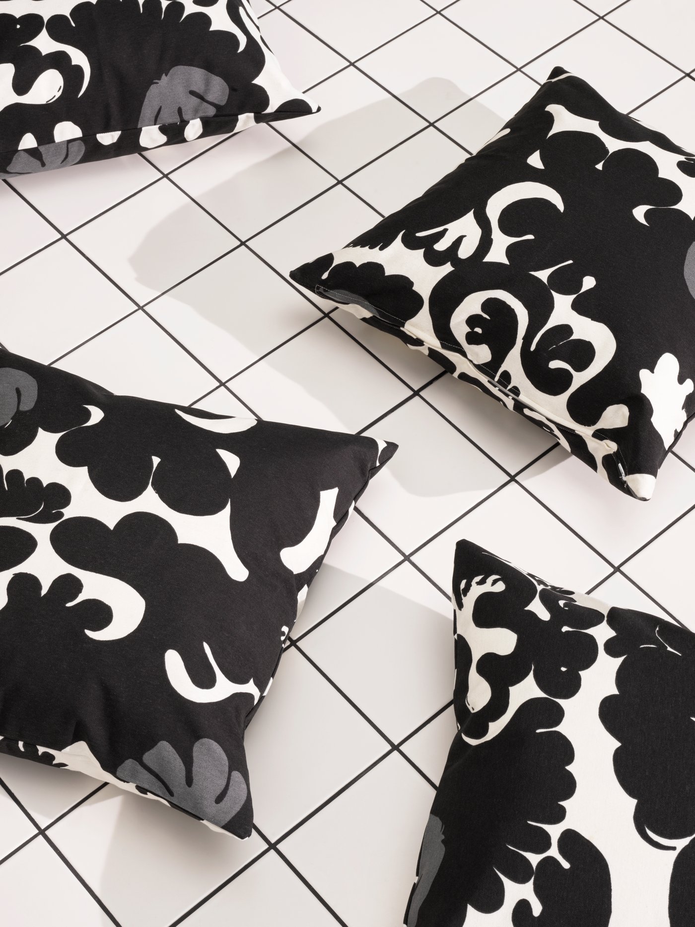 Four cushions in STRECKFLY black and white cushion covers lie scattered over a white tiled floor with black joints.