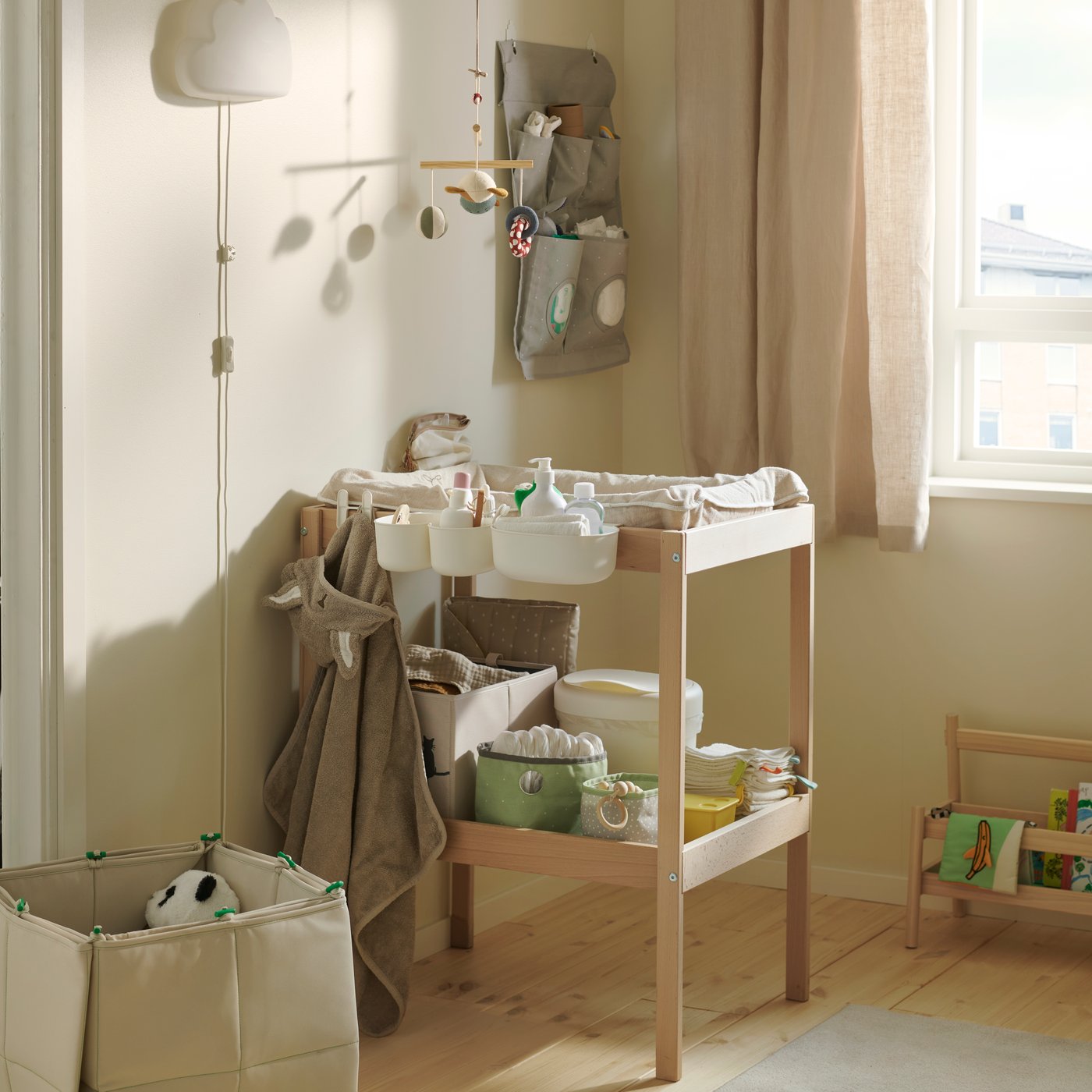 A nursery with beige walls and a SNIGLAR changing table, its shelves stocked with nappies and baby items.