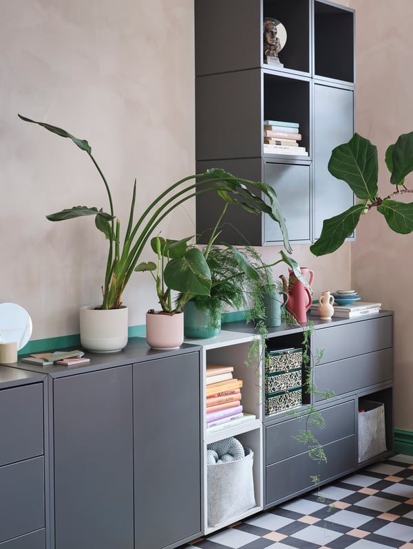 Sleek grey and white cabinets with shelves, drawers and doors. Green plants are displayed on top of the lower cabinets.